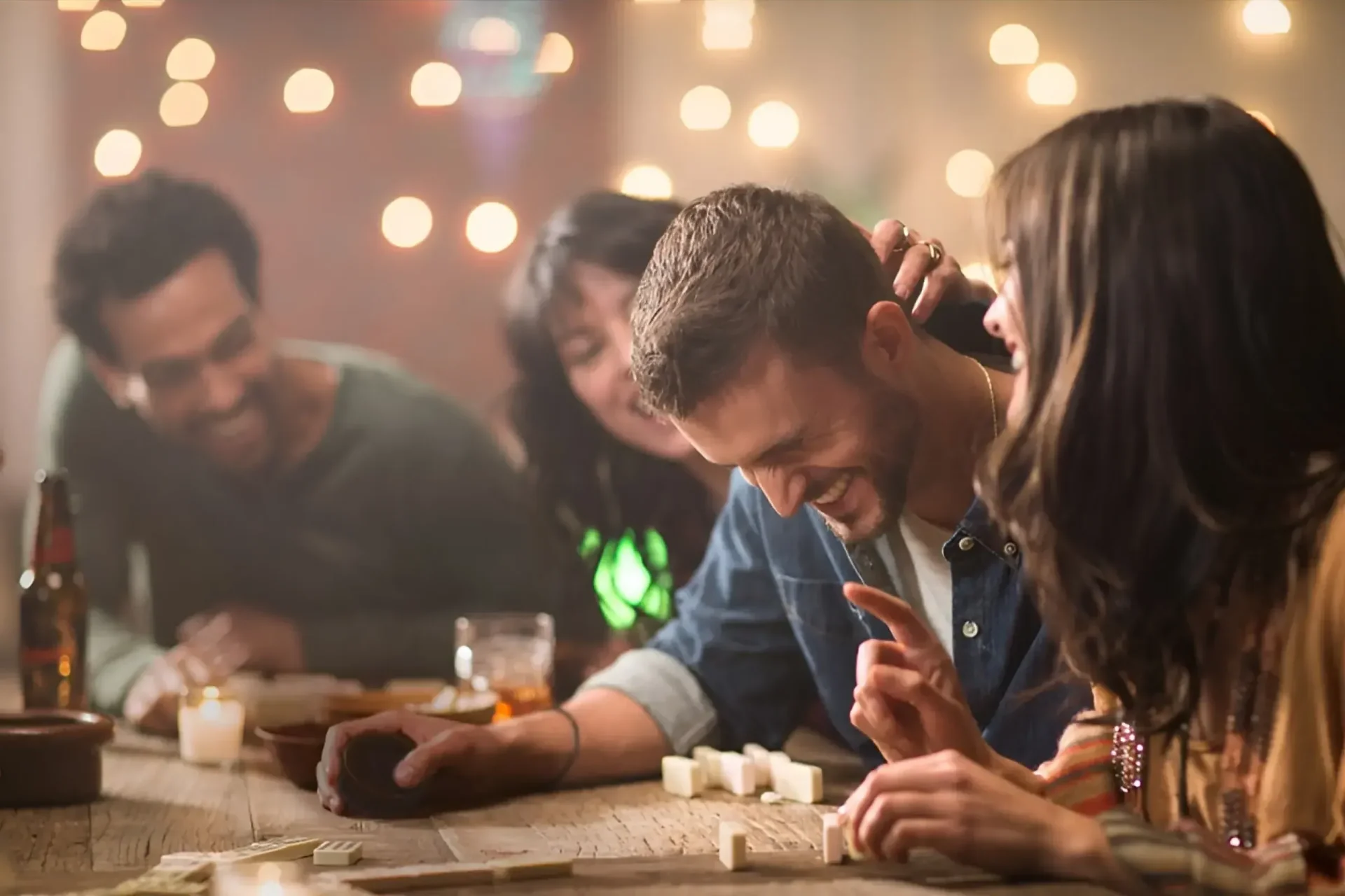 Friends laughing and playing dominoes around a candlelit table